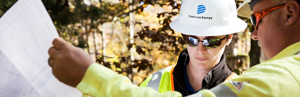 Two Dominion Energy employees in hard hats, reviewing schematics