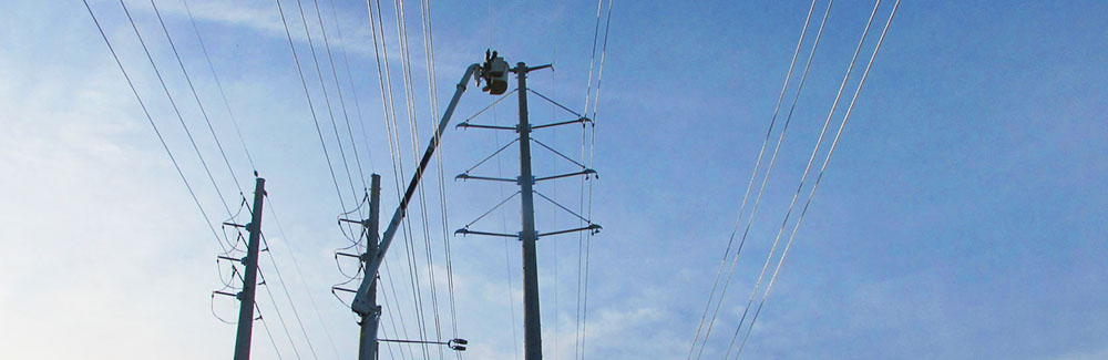 An employee in a bucket truck works on power lines with a blue sky in the background