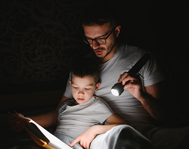 Dad and son reading by flashlight