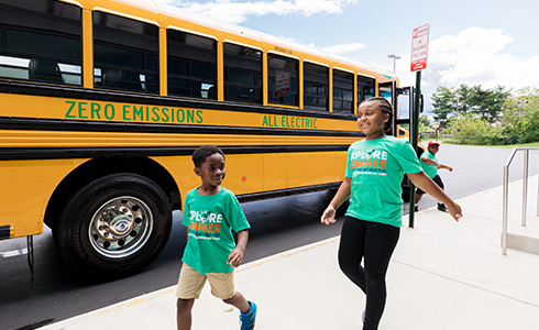 two girls running beside electric bus